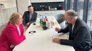 Bärbel Bas in a pink blazer talking with two men at a white table in an office kitchen; one man is writing notes