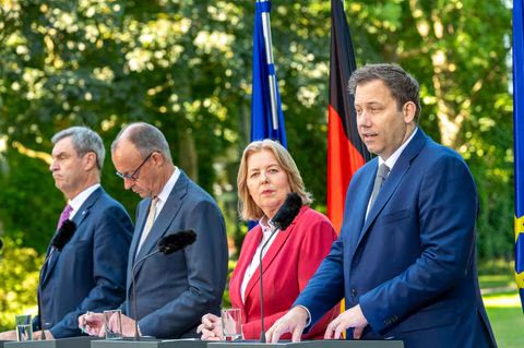 Markus Söder, Friedrich Merz, Bärbel Bas and Lars Klingbeil standing at lecterns outdoors in front of German and EU flags at a press conference