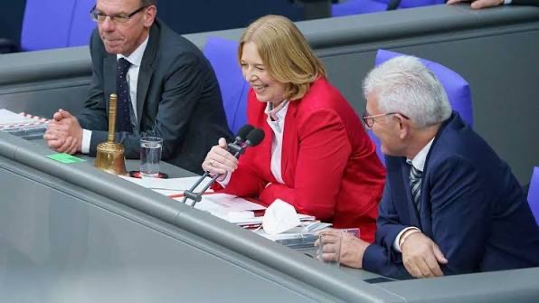 Bärbel Bas laughing at the presiding desk between two colleagues; a brass bell stands on the desk